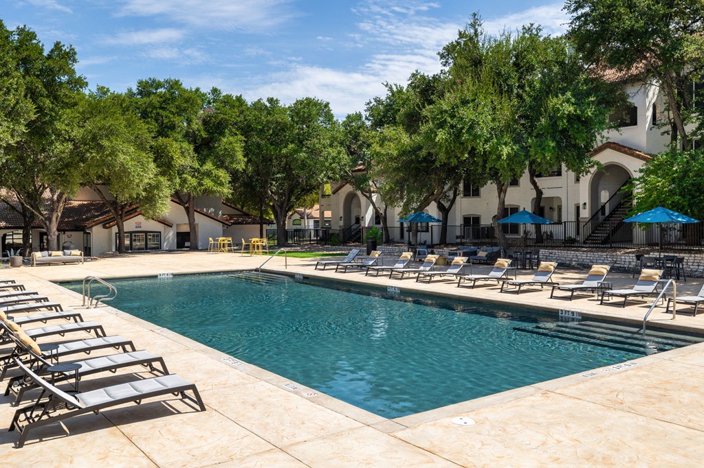 a swimming pool with lounge chairs and trees in the background