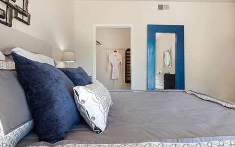 Bedroom with an upholstered headboard, a leaning blue-framed mirror and an open doorway through to the closet.