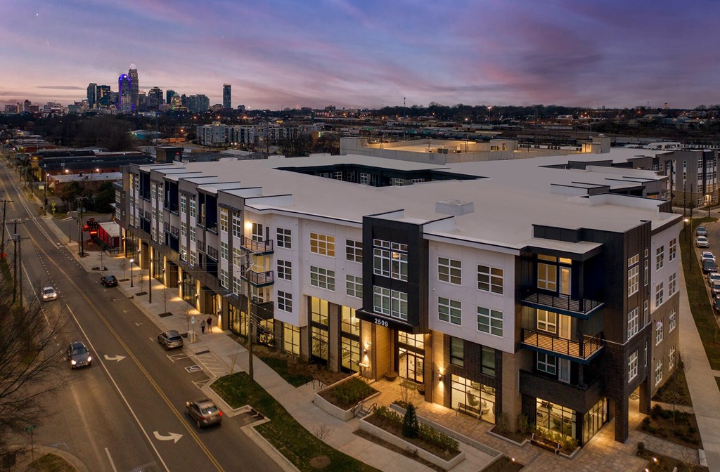 A modern apartment complex is shown with cars parked in the parking lot.