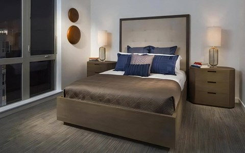 Bedroom with a tall tufted headboard, two wood nightstands, matching table lamps and a wide window beside the bed.