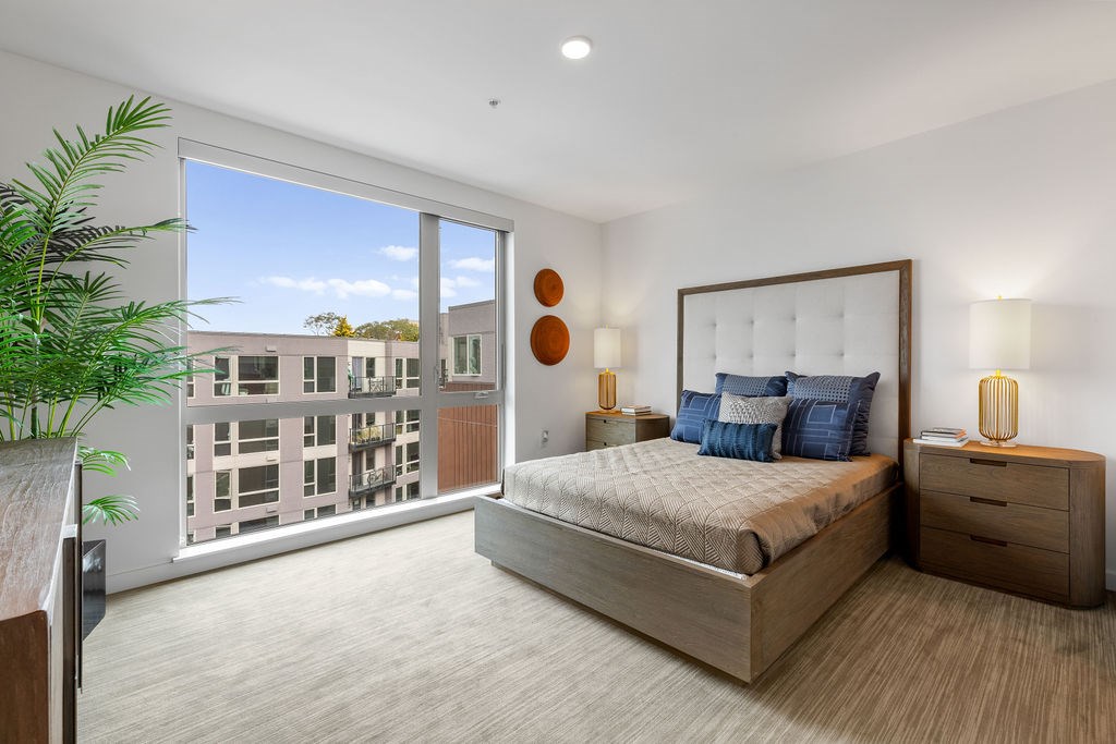A bedroom with a large bed, a dresser, and a balcony with a view of a building.