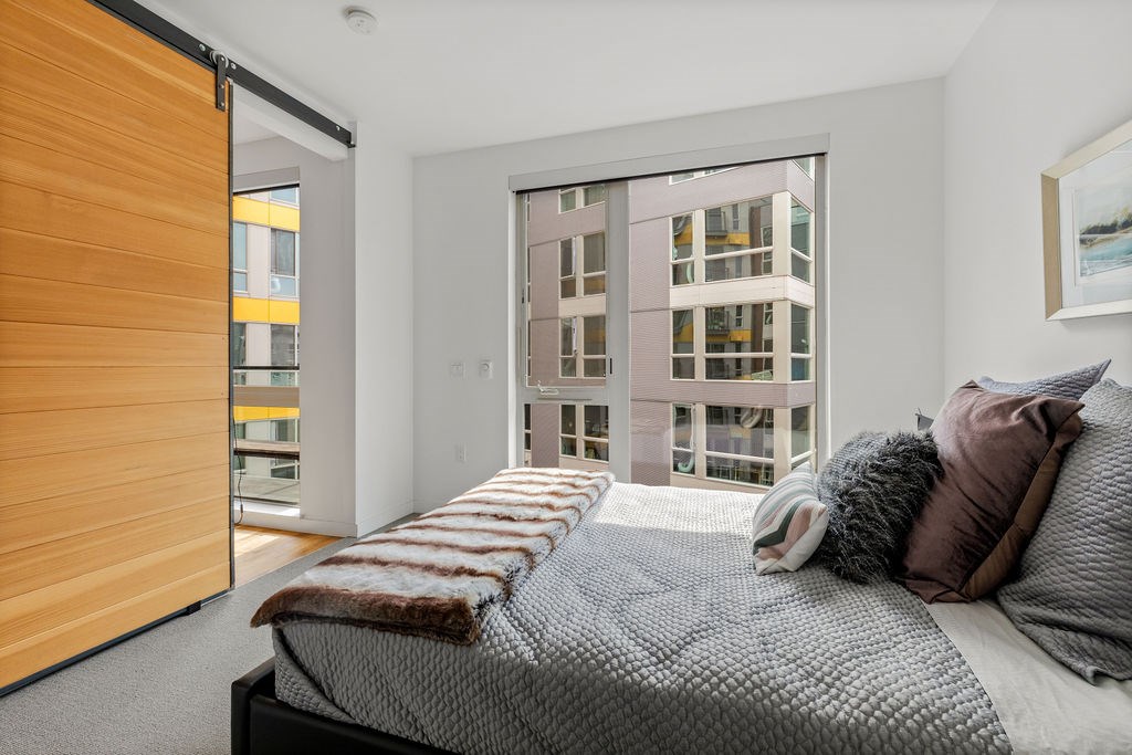 A bedroom with a large bed and a view of a building outside the window.