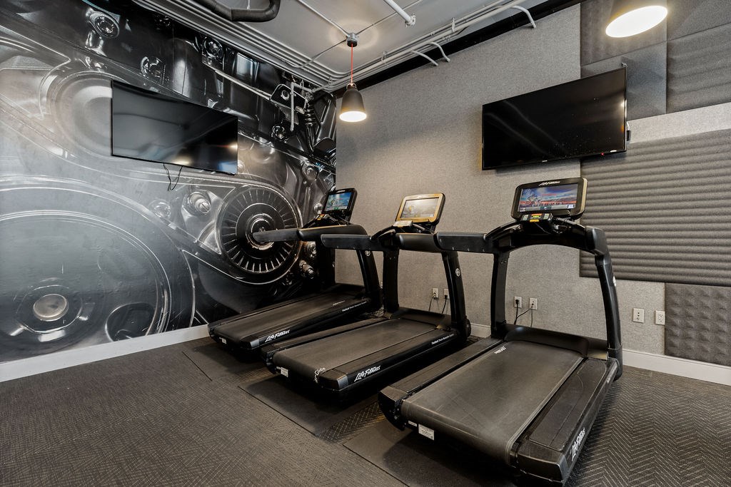 A treadmill and a stationary bike in a gym with a car-themed wallpaper.