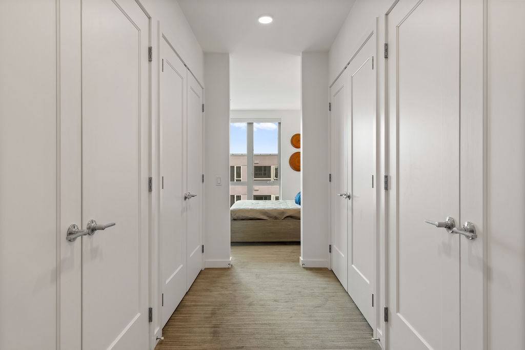 A long hallway with white doors and a bedroom at the end.