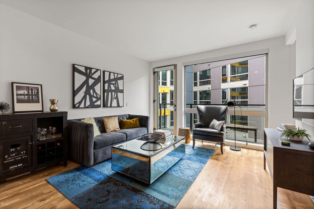A living room with a grey couch, a black cabinet, a glass table and a blue rug.