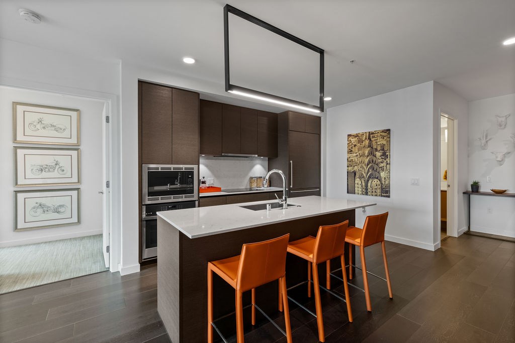 A modern kitchen with a white island and orange chairs.