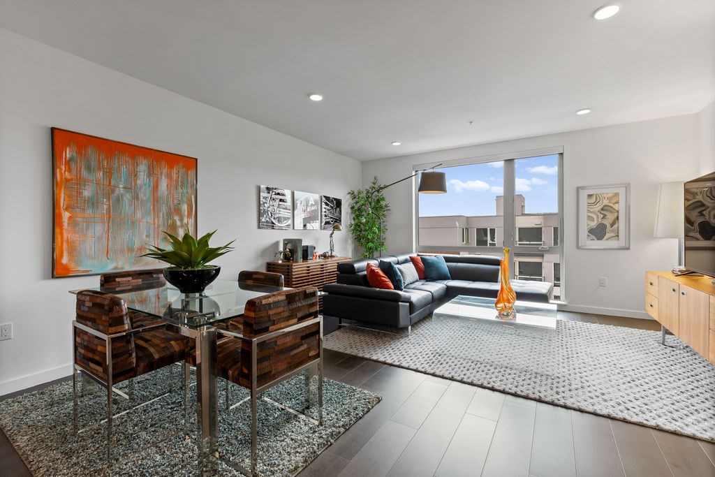 A modern living room with a glass table and a large painting on the wall.