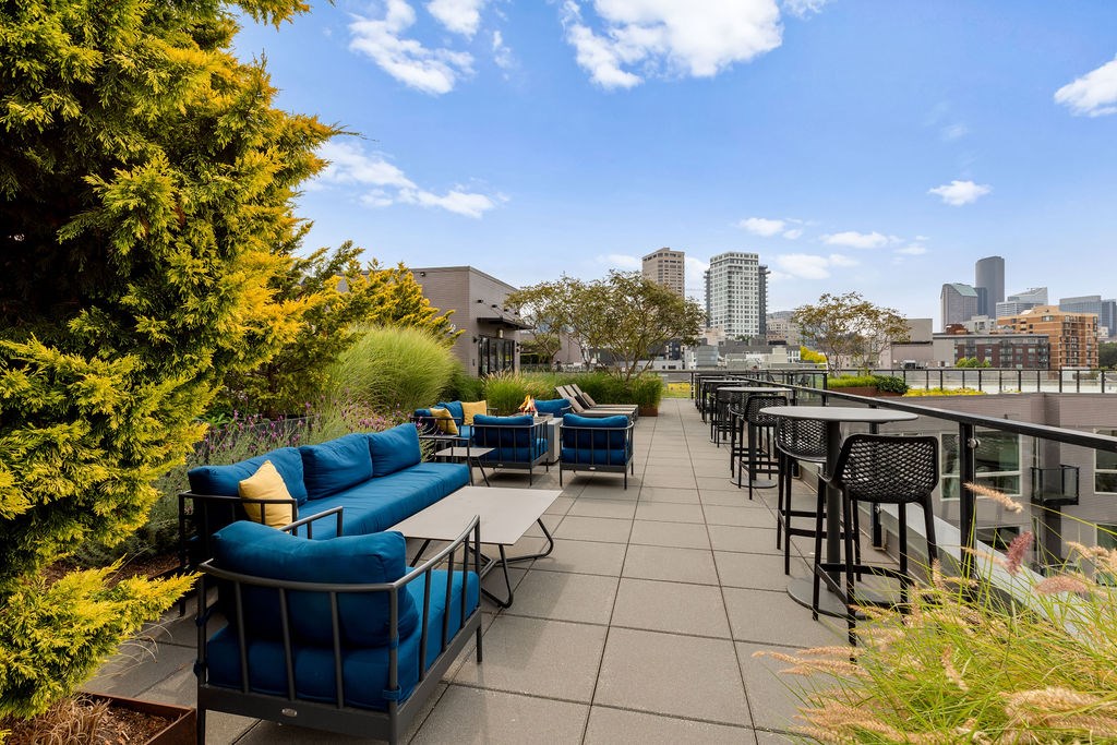 A rooftop patio with blue couches and chairs overlooking a city skyline.