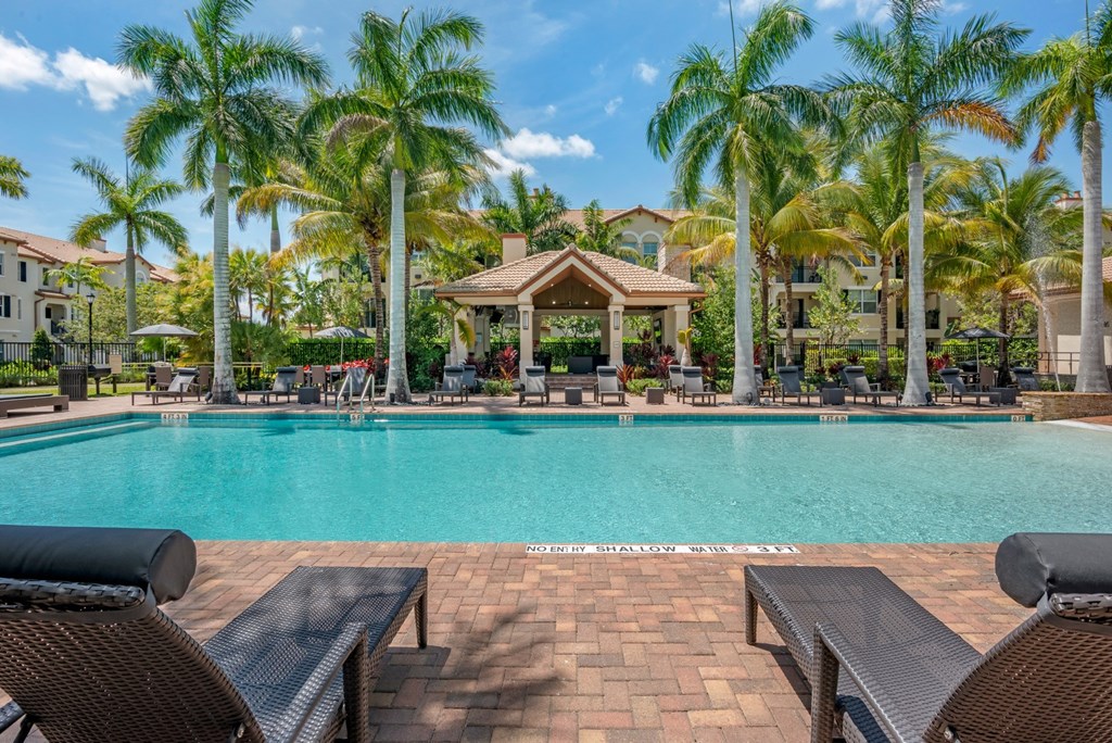 A pool surrounded by palm trees and lounge chairs.