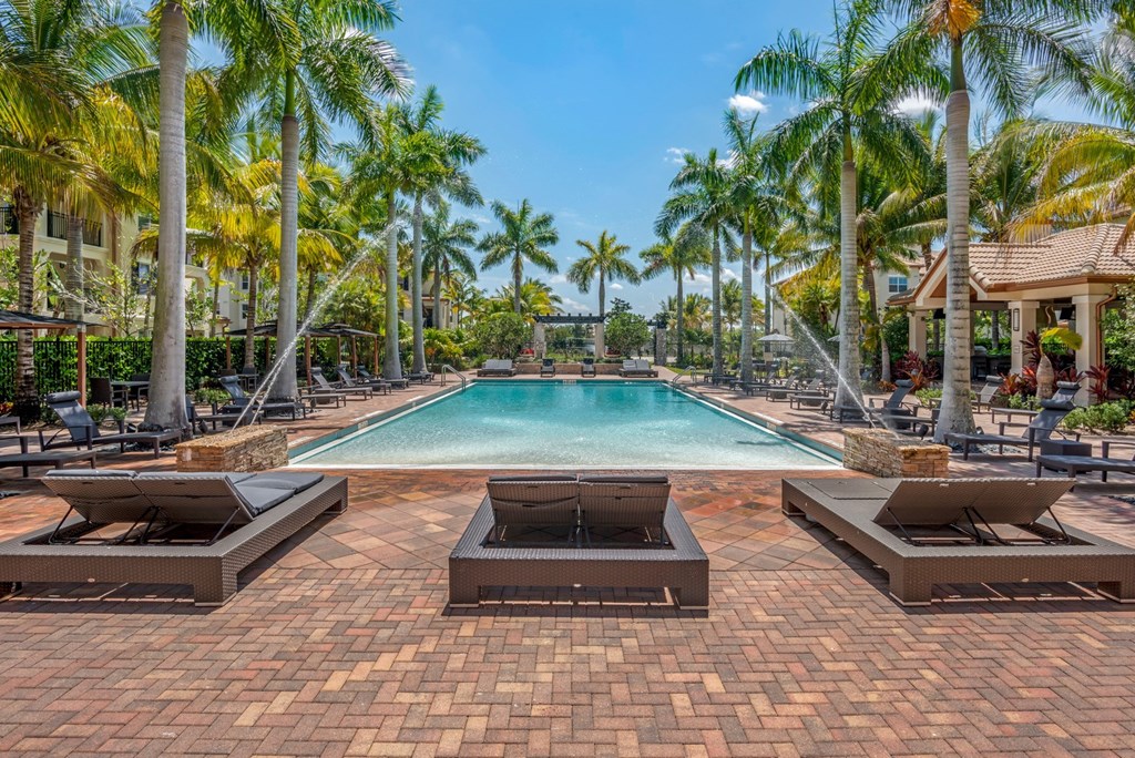 A pool surrounded by palm trees and lounge chairs.