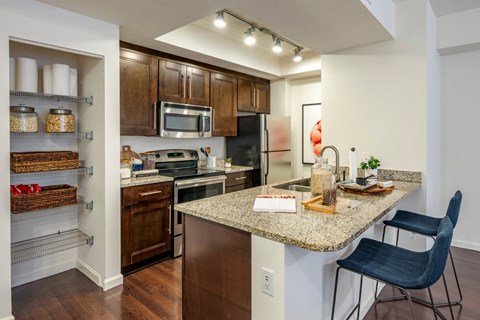 Kitchen with dark wood cabinets, granite counters, stainless appliances and a granite peninsula with two stools.