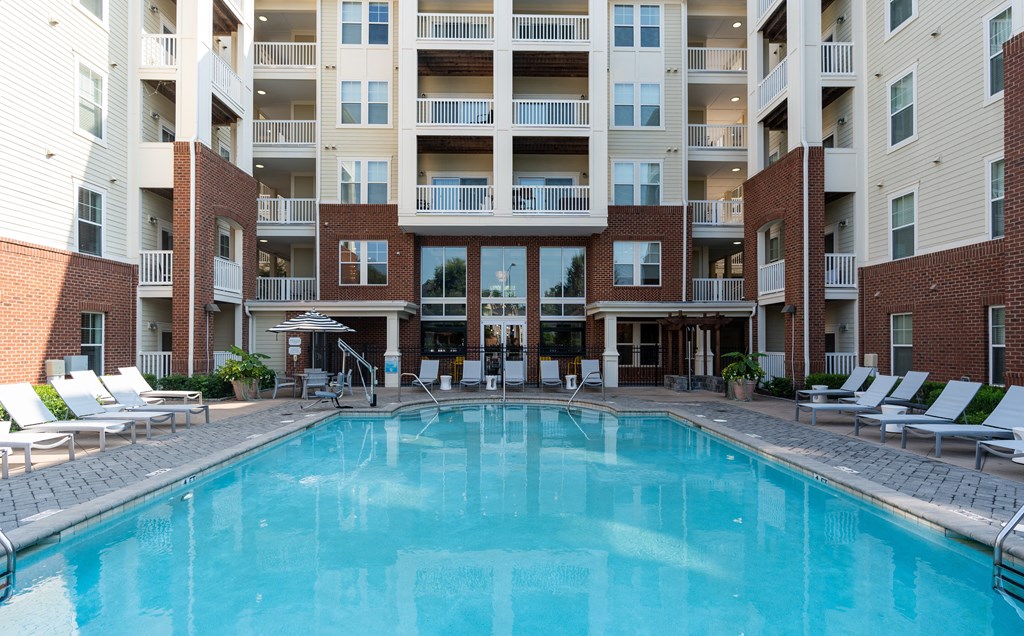 Modern Apartment Pool Area Featuring Sun Loungers and Umbrella-Shaded Tables