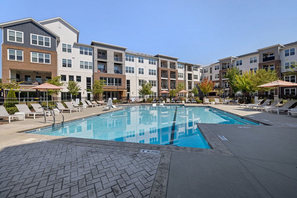 A swimming pool surrounded by apartment buildings and lounge chairs.