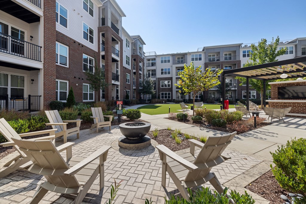 A patio with chairs and a fire pit in front of apartment buildings.