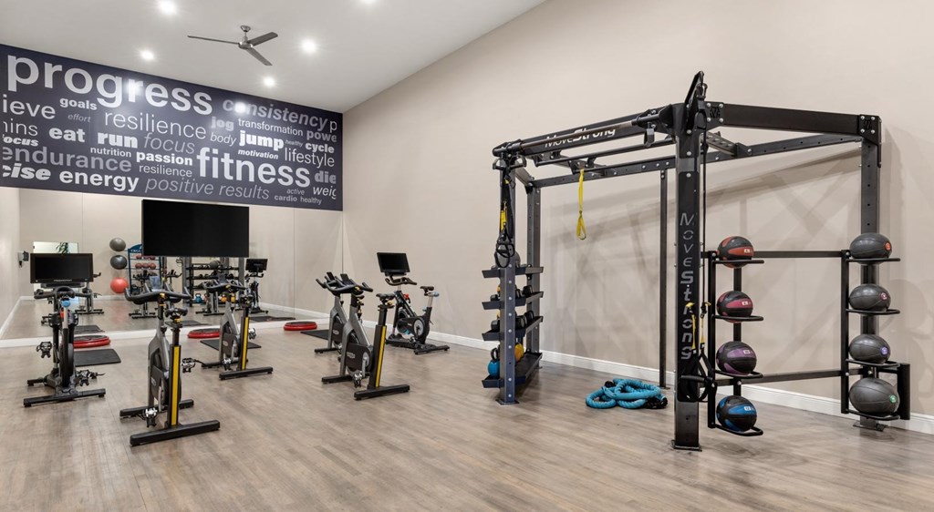 A gym with a variety of equipment including a squat rack, dumbbells, and exercise bikes.