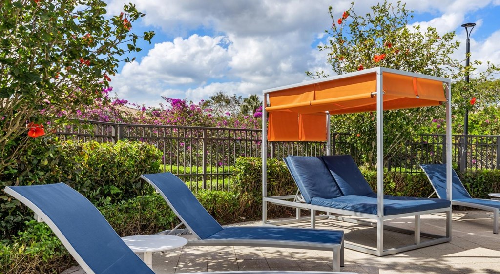 A sun lounger with a blue cushion and a white frame is in front of a fence and some trees.