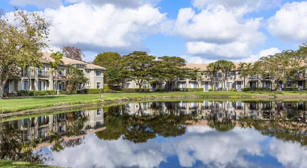 A serene lake in front of a row of houses with trees in the background.