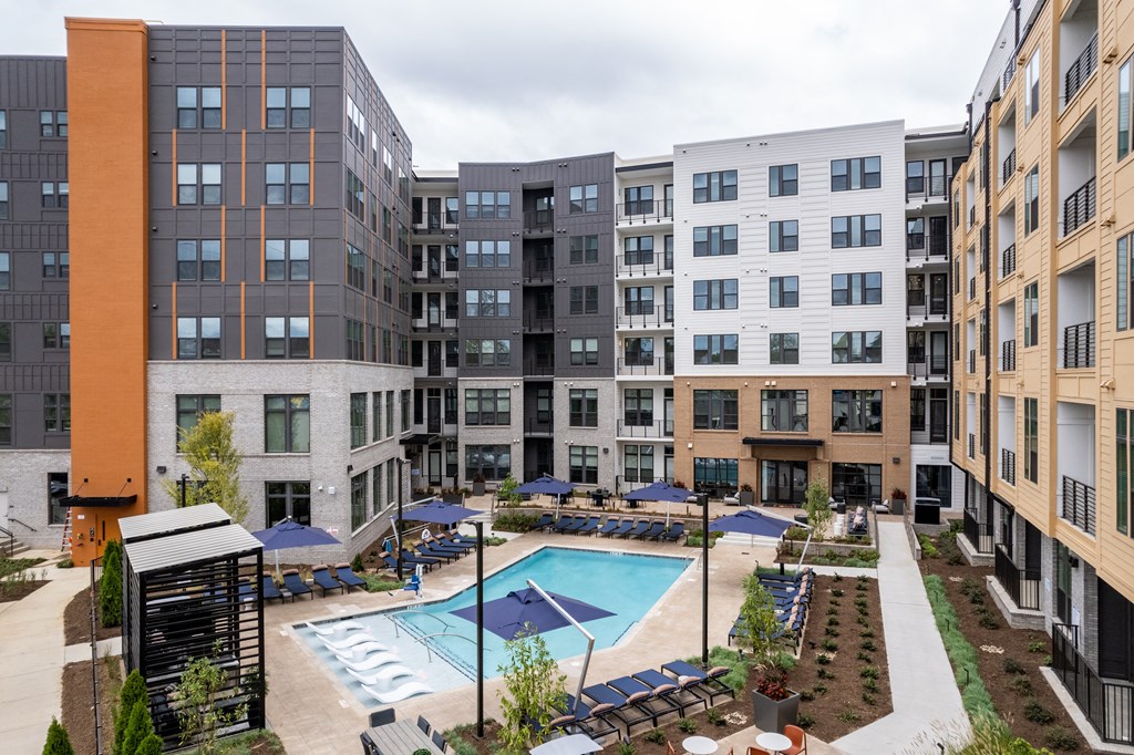A large swimming pool is surrounded by a patio with lounge chairs and umbrellas.
