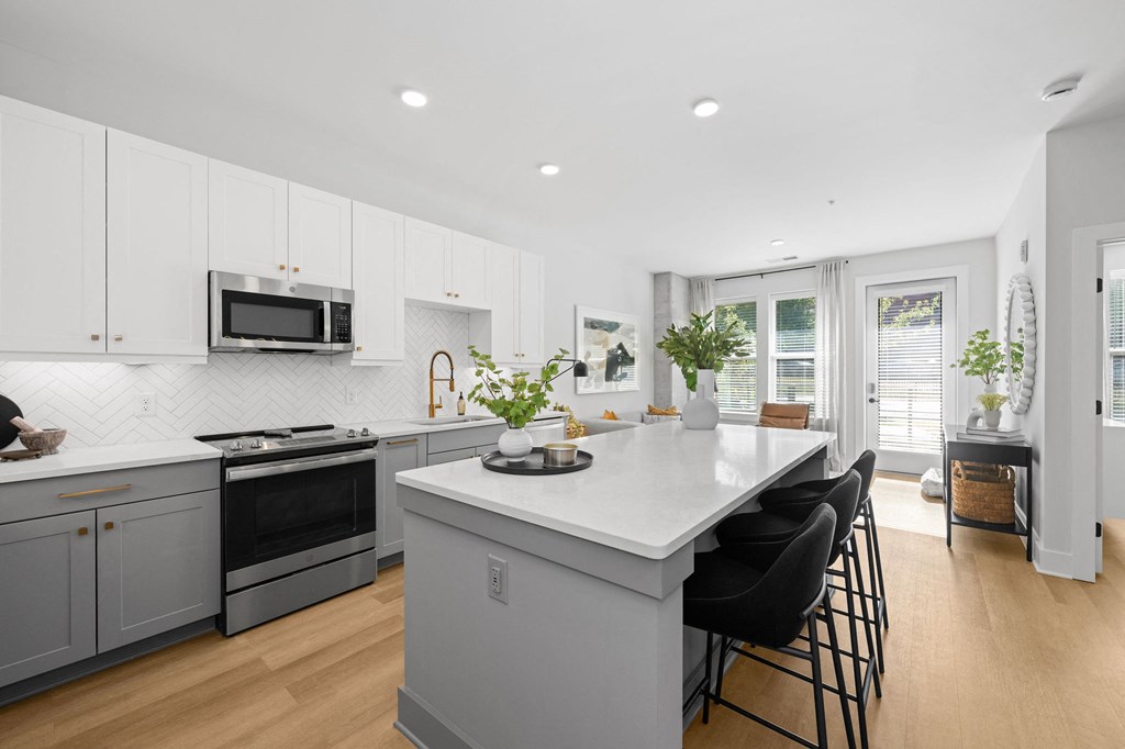 A kitchen with a white island and black chairs.