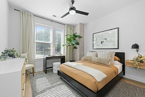 A bedroom with a bed, desk, chair, and a ceiling fan.