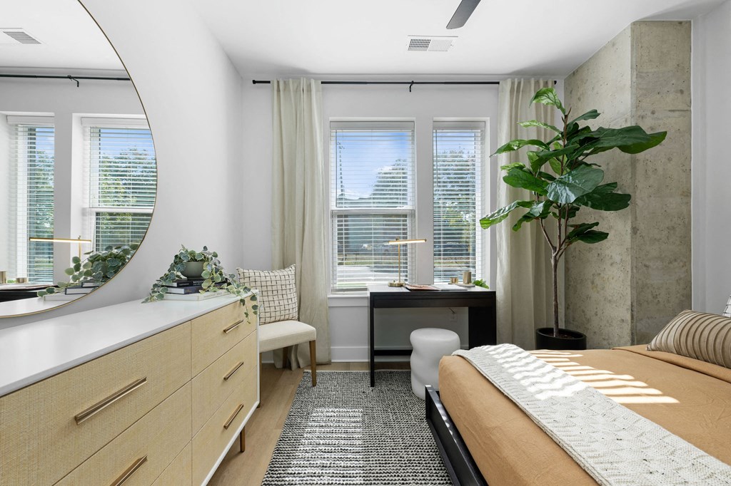 A bedroom with a large bed, a desk with a chair, and a window with a view of the city.