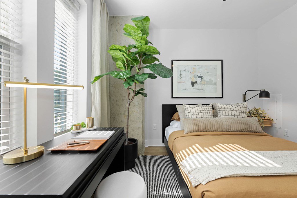 A bedroom with a bed, desk, and a potted plant.