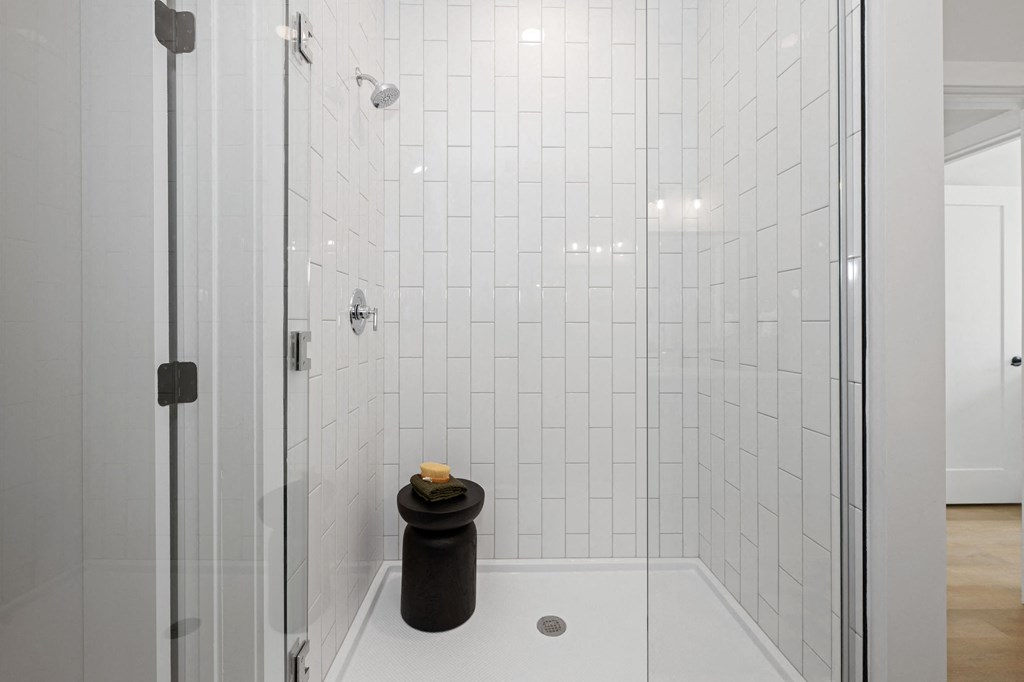 A black trash can sits in a white tiled shower.