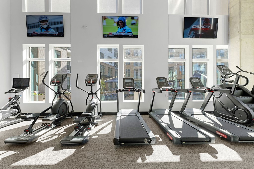 A gym with treadmills, exercise bikes, and televisions showing sports.