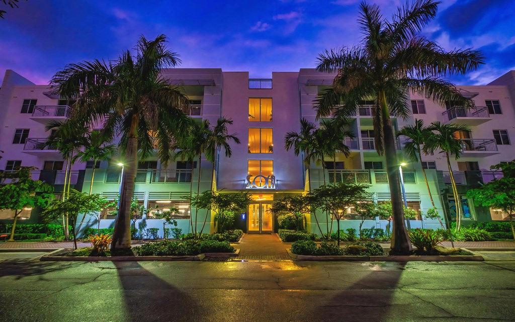 Exterior View of Apartment Building at Dusk Framed by Palm Trees and Lit Entry Path