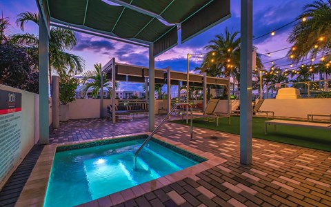 Lit hot tub under a canopy at dusk, with a handrail, string lights and palm trees against a deep purple sky above the deck.