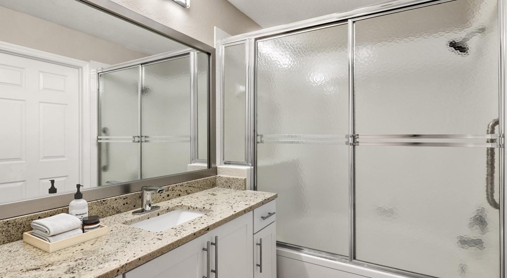 A bathroom with a sink, mirror, and shower.