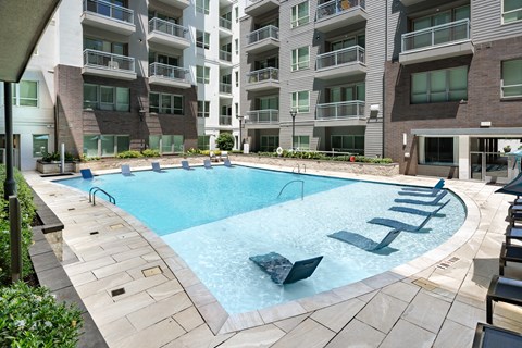 Swimming pool with a shallow tanning shelf holding in-water lounge chairs, edged by a stone deck and balconies.