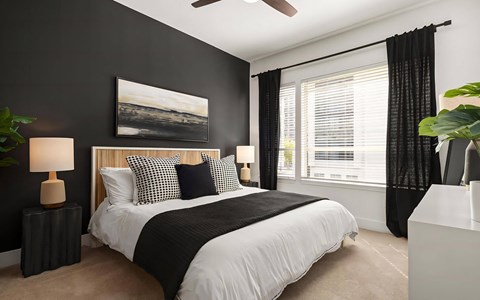 Bedroom with a charcoal accent wall, a fluted headboard, framed landscape art, a ceiling fan and a wide window.