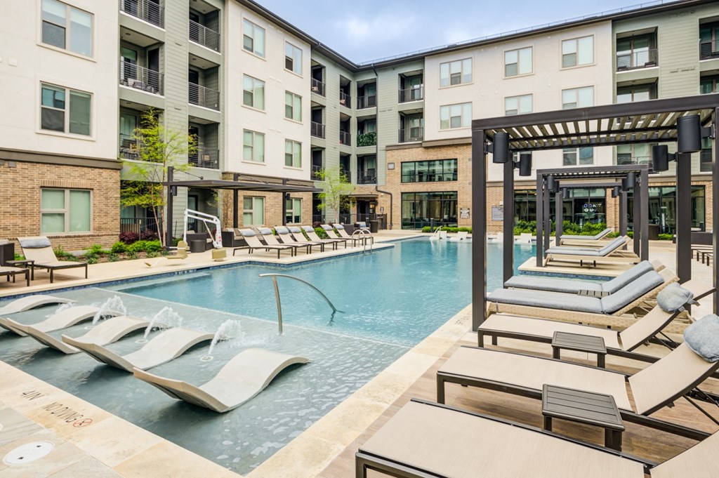 a swimming pool with lounge chairs in front of an apartment building