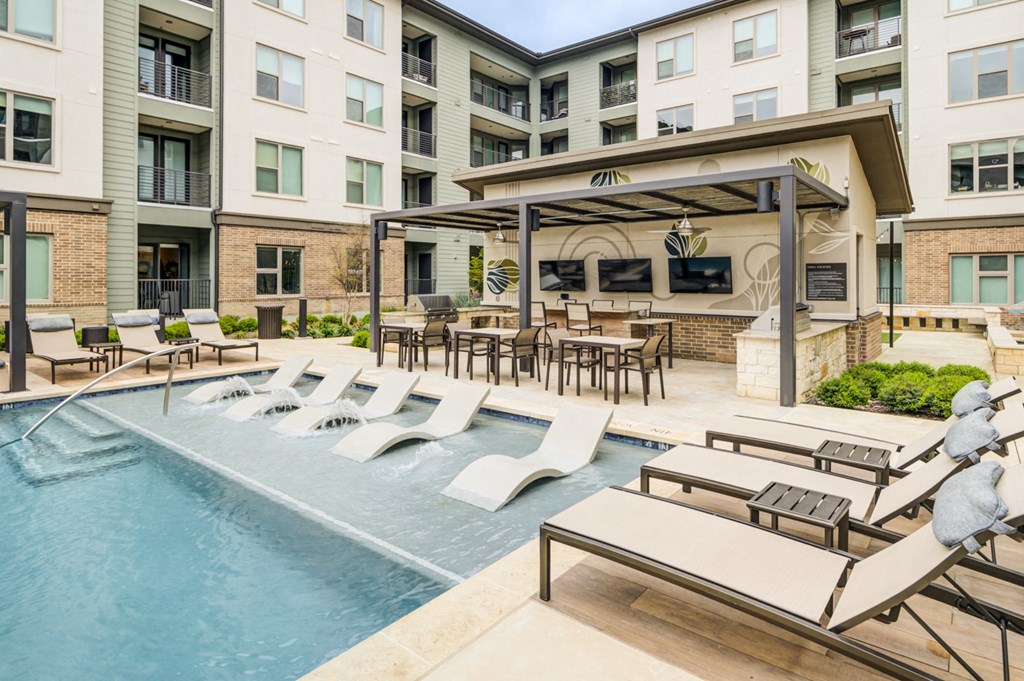 a swimming pool with lounge chairs and tables in front of an apartment building