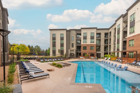 Swimming pool with a marked lap lane, a long row of chaise lounges on the deck, and the courtyard building behind.