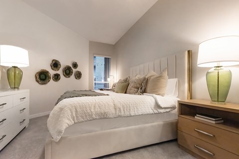 A bedroom with a large bed, a nightstand with a lamp, and a dresser with a lamp.