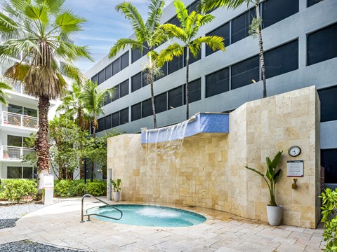 A pool surrounded by a stone wall and palm trees.