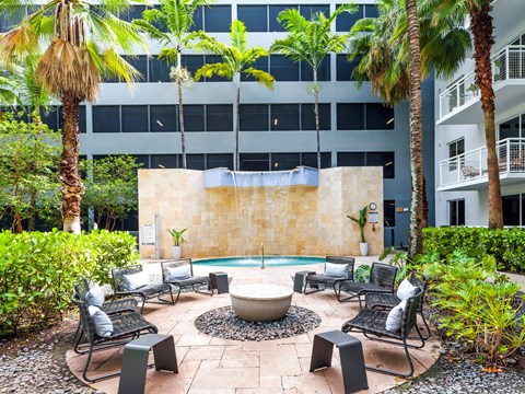 A patio with a fire pit surrounded by chairs and plants.