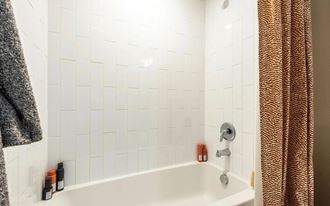 a white tiled bathroom with a tub and a shower curtain