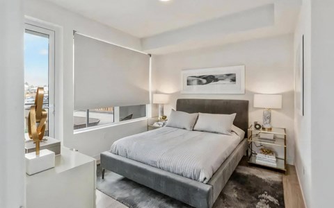 Bedroom with a grey upholstered bed, mirrored nightstands and a glass door opening onto a private balcony off the bedroom.