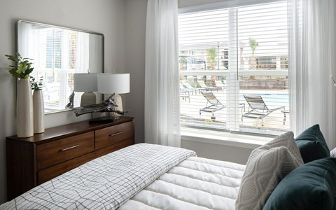 Bedroom with an upholstered headboard, teal cushions, framed abstract art and a window over the pool deck and its loungers.