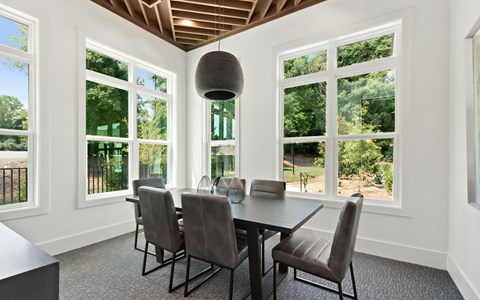 Workspace with a dark table and six leather chairs, a woven pendant and windows on three sides to the trees outside.