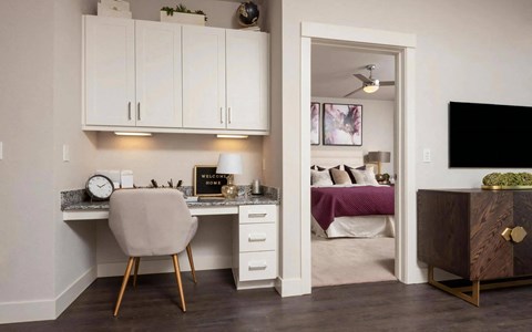 Built-in desk with a granite top, white cabinets above and an open doorway through to the bedroom beyond and its ceiling fan.