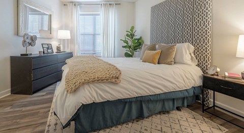 Bedroom with a patterned accent panel behind the bed, a black dresser, matching lamps, and a curtained window.