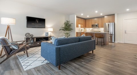 Living area open to the kitchen, with a blue sofa, a mounted television, and an island with counter seating beyond.