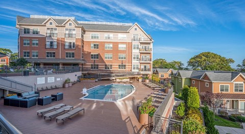 Resort-style pool at Arlington 360 on a wide wood sundeck, with lounge chairs and the brick building rising behind.