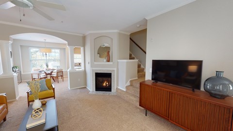 Living room with fireplace, staircase, bay-window dining area, and television.