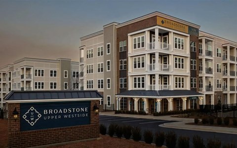 Lantern-lit brick monument sign for Broadstone Upper Westside, with the four-story leasing building behind it.
