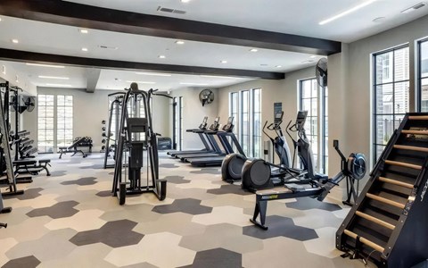 Fitness center with treadmills, ellipticals, a rower, a stair climber, and a cable machine under tall windows.